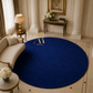 A large round royal blue area rug displayed in an elegant, classic living room with white columns, a cream sofa, and a console table. The brand name 'Artista Rug' is printed in gold on the rug.