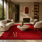 A luxurious red area rug with a gold monogram logo and white dotted border details, styled in a modern, elegant living room with cream-colored furniture and a stone fireplace.