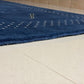 A close-up of a dark blue textured rug with a geometric dotted pattern and a gold monogram logo, shown on a light beige tiled floor.