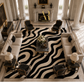 A large area rug with a bold black and cream wavy abstract pattern, styled in a luxurious, high-ceilinged classic living room with cream sofas, black armchairs, and marble tables.