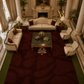 An overhead view of a luxurious living room featuring a large deep burgundy area rug with an abstract organic pattern, styled with cream-colored sofas, armchairs, a green marble coffee table, and classic columns.