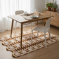 Dining table with chairs on a patterned rug in a room with light curtains and wooden furniture.
