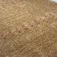 A close-up of a textured area rug with a heathered tan and brown base, accented by small magenta geometric and floral motifs.