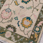Close-up of a patterned rug with floral designs in green, pink, and yellow on a neutral background.