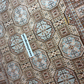 Close-up of a patterned rug with geometric design, featuring a brand label.