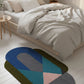 Colorful geometric rug on a light wooden floor in a bedroom setting.
