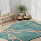 Teal rug with pink patterns on a wooden floor, with a bench and plants in the background.