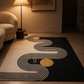 A modern area rug with a black background, cream wavy geometric lines, and two gold circular accents, styled in a warm, contemporary living room next to a beige armchair and a lit floor lamp.
