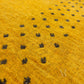Close-up of a mustard yellow textured fabric with a repeating pattern of small black embroidered or woven dots.