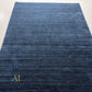 A dark navy blue area rug with a subtle horizontal textured pattern and a small gold monogram logo in the bottom right corner, shown against a plain white background.