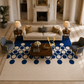 A large modern area rug in cream and navy blue with a bold circle pattern, styled in a luxurious, symmetrical classical living room with a cream sofa, blue armchairs, and a wooden coffee table.