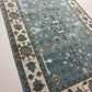 Blue patterned rug with white border on a light gray floor