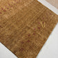 A rectangular brown area rug with a textured, heathered finish, featuring horizontal bands of small red geometric motifs and a central gold Om symbol near the bottom.