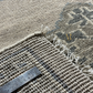 Close-up of a textured rug with a ruler for scale, featuring a brand logo.