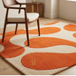 Orange and beige abstract rug on a marble floor with chairs around a table.