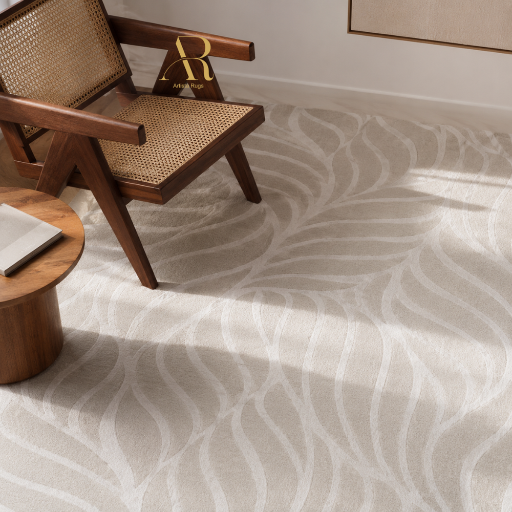A light beige area rug with a white wavy leaf pattern, styled in a modern room with a wooden armchair and a small wooden side table.