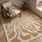 A large area rug with a beige and cream abstract wavy pattern, styled in a modern living room setting next to a wooden armchair and a rustic vase.