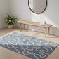 Blue and white patterned rug on a wooden floor with a wooden bench and plant in the background.