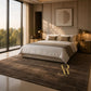 A styled bedroom scene showing a bed with white bedding and a brown textured area rug in a modern, warm-toned room. A large gold 'R' logo with 'Rustico Rug' is printed on the rug.
