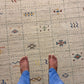 Close-up of a textured area rug with a cream-colored base, featuring a central rust-brown abstract symbol and scattered blue and gray motifs.