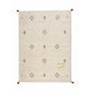 A rectangular beige area rug with a Southwestern geometric pattern in brown, gold, and black, featuring a gold monogram logo near the bottom right. The rug is shown flat against a solid white background.