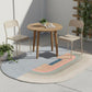 Round wooden table with two chairs on a colorful rug in an outdoor setting.