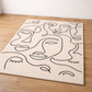 Beige rug with black line art of faces on a wooden floor