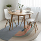 Dining area with a round wooden table and white chairs on a colorful rug.