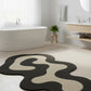 Modern bathroom with a black and beige abstract rug on a light wood floor.