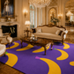 A large purple area rug with bold yellow banana-shaped patterns and small green and pink accents, shown in a luxurious vintage-style living room with an ornate cream sofa, wooden coffee table, and crystal chandelier.