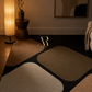 A modern area rug with an abstract geometric pattern in beige, brown, and black, styled in a warm, dimly lit living room next to a glowing floor lamp.