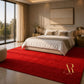 A large, plush red area rug in a modern, warm-toned bedroom. The rug features a gold 'Artful Rug' logo in the bottom right corner.