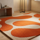 Orange and beige patterned rug on a wooden floor with a side table and lamp in the background.