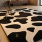 Black and white patterned rug with a brand logo on a wooden floor.