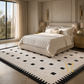 A large rectangular area rug with a black and off-white geometric pattern, styled in a modern, elegant bedroom setting.