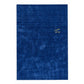 A rectangular royal blue textured rug with a small gold embroidered monogram logo in the upper right quadrant, shown flat against a plain white background.