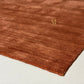 A close-up of a rust-brown textured rug with a small gold embroidered letter 'AR' on a light-colored floor.