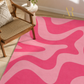 A pink and light pink wavy abstract patterned area rug styled in a modern room setting next to a wooden cane armchair.