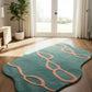 Teal rug with pink patterns on a wooden floor in a room with large windows and a plant.