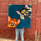 Person holding a cartoon-themed blanket with characters against a brick wall.