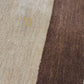 A close-up of a brown area rug with vertical stripes in beige and a muted blue-gray, shown with a person's hand and wrist resting on the surface. A gold 'R' logo is printed on the rug.