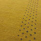 Close-up of a mustard yellow textured fabric with a repeating pattern of small black embroidered or woven dots.