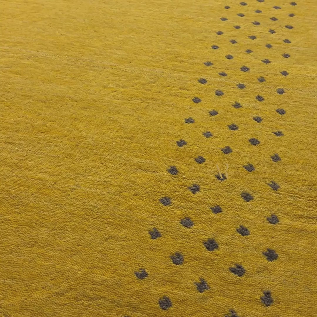 Close-up of a mustard yellow textured fabric with a repeating pattern of small black embroidered or woven dots.