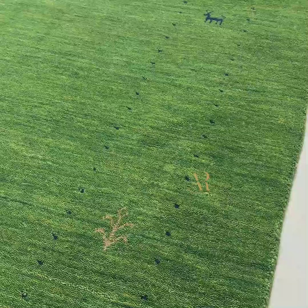 Green artificial turf or grass-like flooring material shown in a close-up, with a folded section revealing the backing and a small white monogram logo.
