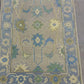 Close-up of a patterned rug with floral designs in blue, green, and beige on a gray background.