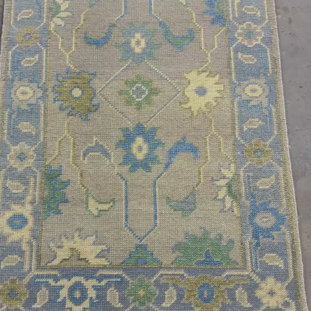 Close-up of a patterned rug with floral designs in blue, green, and beige on a gray background.