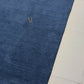 A rectangular royal blue textured rug with a small gold embroidered monogram logo in the upper right quadrant, shown flat against a plain white background.