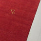 A rectangular red rug with a textured plush surface, featuring a gold monogram logo and the brand name 'Artemio Ruga' in the top-left corner, set against a plain white background.