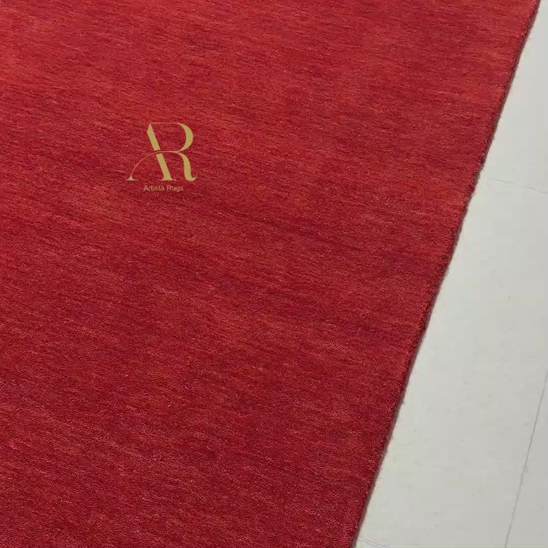 A rectangular red rug with a textured plush surface, featuring a gold monogram logo and the brand name 'Artemio Ruga' in the top-left corner, set against a plain white background.