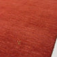 A rectangular area rug in a rich rust red color with a subtle textured pattern and a small gold butterfly motif in the upper left quadrant, shown against a plain white background.
